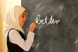 Muslim girl writing the word "better" on a blackboard