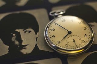 Close-up of a watch face resting on a portrait photo of a young Paul McCartney, from The Beatles, whose eyes seem to be looking at the watch.